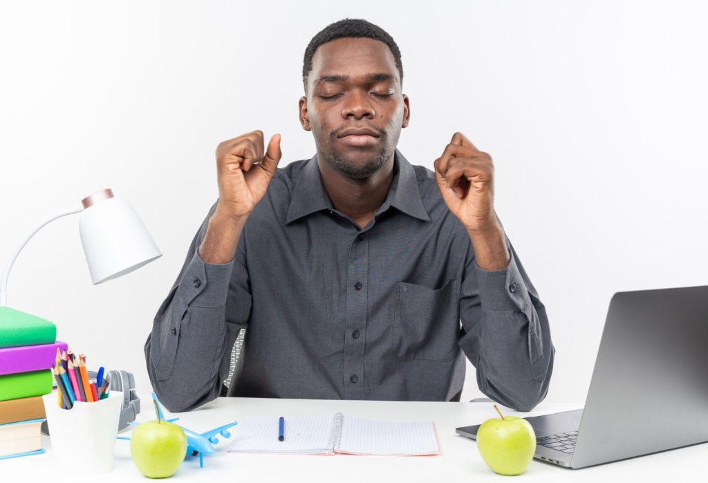 Jeune étudiant afro-américain anxieux assis les yeux fermés au bureau ave